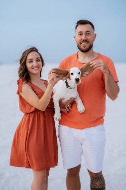 Turuncu elbiseli genç çift ve köpek çölde beyaz kumlarda
