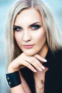 Gri molozlardan yapılmış bir taş ocağının arka planında mavi gözlü siyah pantolonlu sarışın kız.