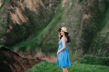 Dağdaki yeşil yamaçlarda geniş kenarlı hasır şapkalı genç kız.