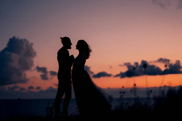 海に沈むオレンジ色の夕日を背景に幸せなカップルの男と女のシルエット — ストック写真