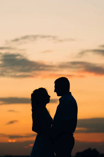 一对快乐的年轻夫妇在大海中的橙色落日背景下的轮廓 — 图库照片