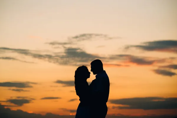 一对快乐的年轻夫妇在大海中的橙色落日背景下的轮廓 — 图库照片