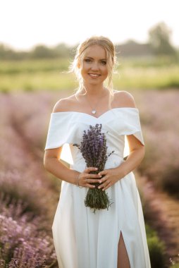 Beyaz elbiseli gelin lavanta tarlasında yürüyor.