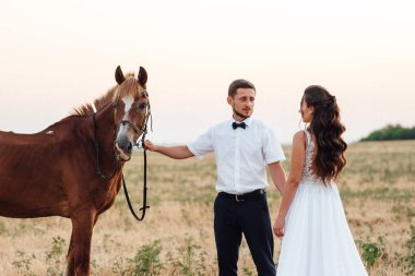 Beyaz elbiseli gelin ve kahverengi atlı beyaz gömlekli damat.
