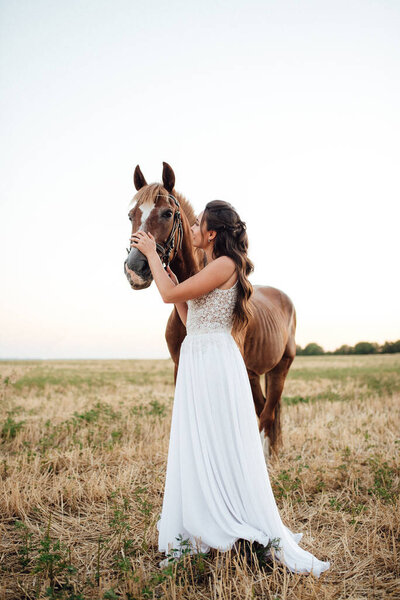 bride in a white dress next to a brown horse in the village