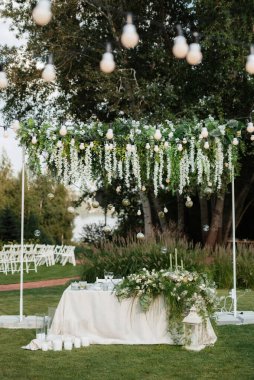 Restoranın ziyafet salonundaki yeni evlilerin başkanlığı mumlar ve yeşil bitkilerle süslenmiş, salkımlar tavandan sarkmış.