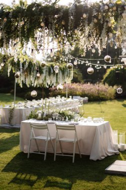 Restoranın ziyafet salonundaki yeni evlilerin başkanlığı mumlar ve yeşil bitkilerle süslenmiş, salkımlar tavandan sarkmış.