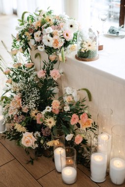 Restoranın ziyafet salonundaki yeni evlilerin başkanlığı mumlar ve yeşil bitkilerle süslenmiş, salkımlar tavandan sarkmış.