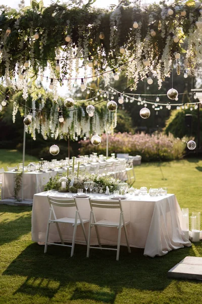 Restoranın ziyafet salonundaki yeni evlilerin başkanlığı mumlar ve yeşil bitkilerle süslenmiş, salkımlar tavandan sarkmış.