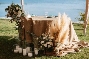 Restoranın ziyafet salonundaki yeni evlilerin başkanlığı mumlar ve yeşil bitkilerle süslenmiş, salkımlar tavandan sarkmış.