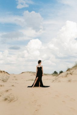 Kumlu çölde, mavi gökyüzünün altında, siyah, uzun elbiseli bir kız.