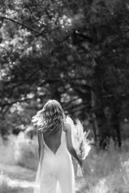 Orman yolunda bir buket kurumuş çiçekle beyaz bir elbise içindeki mutlu gelin kız.