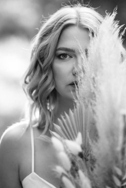 Orman yolunda bir buket kurumuş çiçekle beyaz bir elbise içindeki mutlu gelin kız.