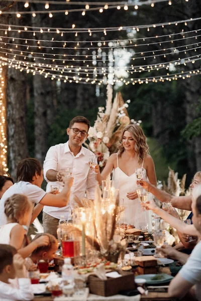 evening wedding family dinner in the forest with light bulbs and candles