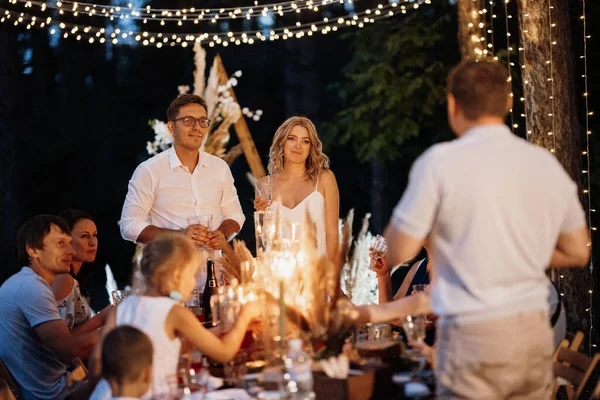 evening wedding family dinner in the forest with light bulbs and candles