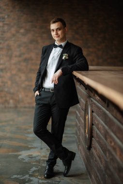 portrait of a young guy groom in a black suit on a rainy day