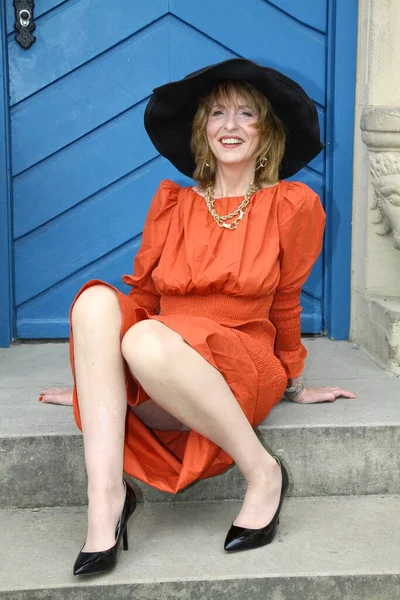 在纽豪斯城堡公园的蓝色大门前 穿着橙色晚礼服的迷人女人摆出一副迷人的姿势 — 图库照片