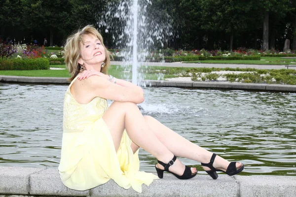 Attraktive Hübsche Frau Sitzt Auf Einer Mauer Vor Einem Brunnen Stockbild