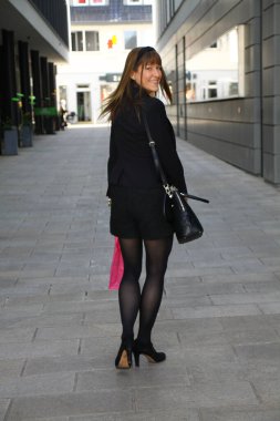 Çekici, şık giyimli bayan bir alışveriş caddesinde yürüyor.