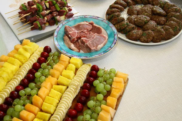 Close-up of fruits and grilled meats, bananas, pineapples, cherries, grapes, melon, meat skewers, lamb chops, meatballs, decorated on a white plate,
