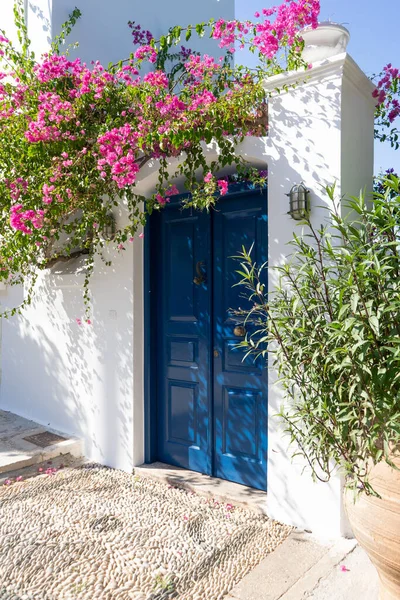 Mavi kapısı ve çiçekli begonvili tipik bir Yunan beyaz binasının cephesi. 