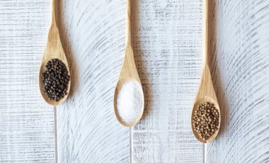 Tahta kaşıklarda tuz, biber ve kişniş, gri arka planda.