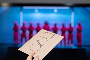 Moskova, Rusya - 19 Ekim 2021. Bir televizyon ekranının arka planında Netflix serisi Squid oyununun logosu olan bir kartla uzanmış bir el.. 