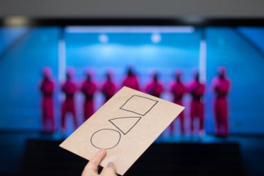 Moskova, Rusya - 19 Ekim 2021. Bir televizyon ekranının arka planında Netflix serisi Squid oyununun logosu olan bir kartla uzanmış bir el.. 