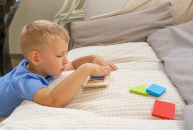 Çocuk ahşap bir masa oyunu oynuyor. Montessori aktivitelerini geliştirmek, şekiller ve geometrik şekiller üzerine çalışmak. Sıralayıcı