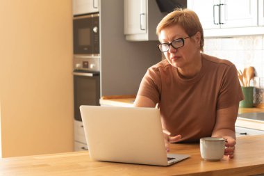Yaşlı bir kadın dizüstü bilgisayarda çalışıyor. Modern teknolojiler ve yaşlı insanlar kavramı. 
