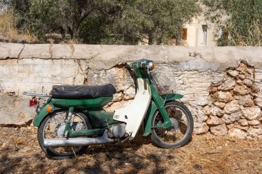 Yunanistan 'da taş bir duvarın arka planında eski yeşil motosiklet