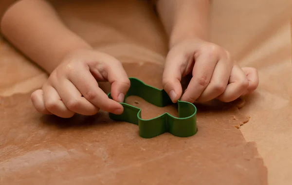 Little childrens hands carve dough with a cookie cutter in the shape of a gingerbread man. Step by step instruction