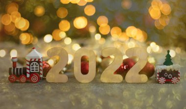 Wooden numbers 2022, toy train and defocus lights of garland.