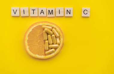 Yarım portakal, multivitamin kapsülleri ve sarı arka planda C vitamini. Doğal vs sentetik vitamin konsepti. 