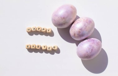 Paskalya konsepti. Beyaz arka planda mor yumurtalar ve ahşap harfler. Peri renginde. Minimalizm. Sert gölgeler.