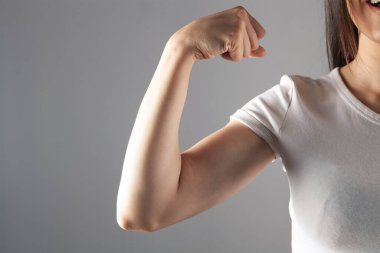 Genç kız kaslarını gri bir arka planda gösteriyor.