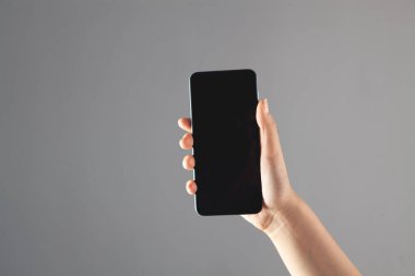 Gri arka planda telefonu tutan genç kadın.