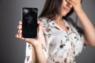 Kırık telefon gösteren genç bir kadın yüzünü kapatıyor.