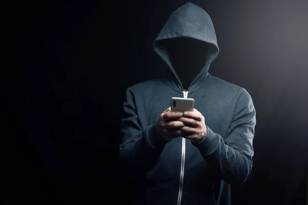 Kapüşonlu bilgisayar korsanı telefonu tutuyor.