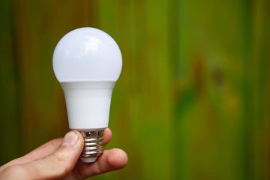 El, yeşil panoların arka planında bir ampul tutuyor.