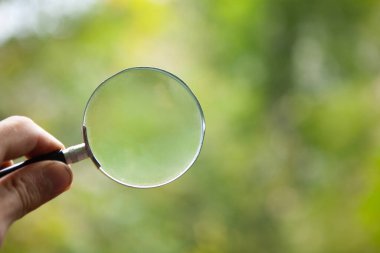 Doğanın arka planında bir büyüteç tutan el.