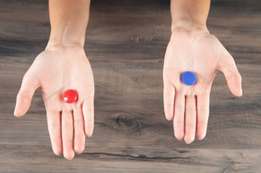 Elinde kırmızı ve mavi haplar tutan bir kadın.