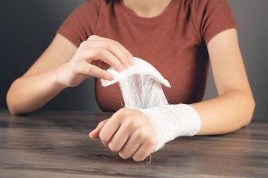Genç bir kadın elini bandajlıyor.