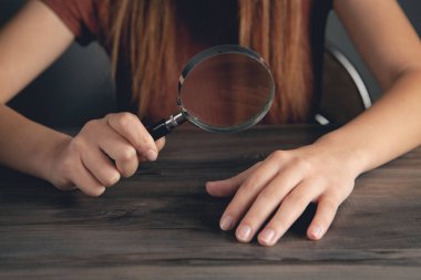 Bir kadın büyüteçle tırnaklarına bakıyor.