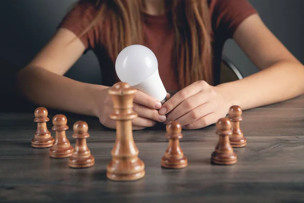 woman holding a light bulb near chess pieces