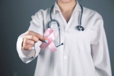 Doktor elinde gri arka planda pembe bir kurdele tutuyor.
