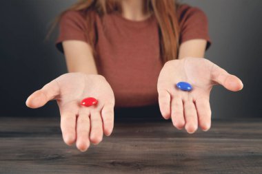 Elinde kırmızı ve mavi haplar tutan bir kadın.