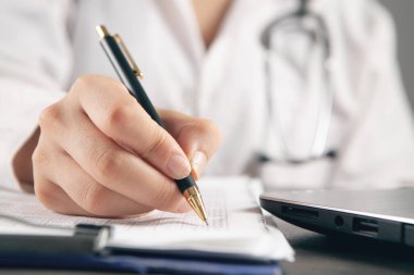 Doktor laptopun önündeki kağıtlara not alır.