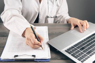 Doktor laptopun önündeki kağıtlara not alır.