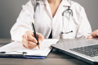 Doktor laptopun önündeki kağıtlara not alır.